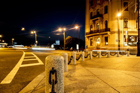 Granite posts with chains. Abstract night city blurred lights of moving cars for decoration design. Yellow background. Abstract background. The dark blue skyの写真素材