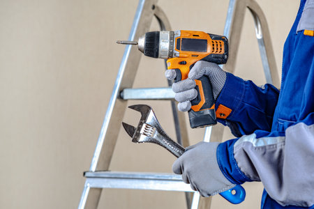 The master is holding an electric screwdriver and a key. Locksmith repair work. The stepladder in the background is ready to goの写真素材