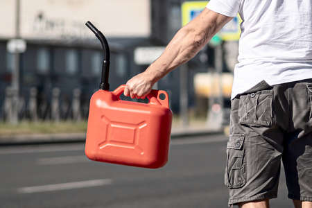 A red canister on the asphalt near the car. The car ran out of gas and stalled. A young man hoping for help on the road from other drivers.の写真素材