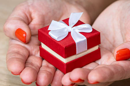 Gift souvenir red box with a bow in the palms of the girl, top view