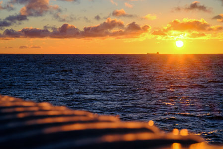 Experience a stunning sunset casting an enchanting glow over ocean waves and sailing shipsの写真素材