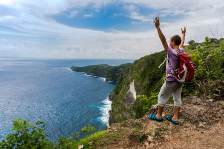 Hiker with backpack standing on top of a mountain with raised handsの写真素材