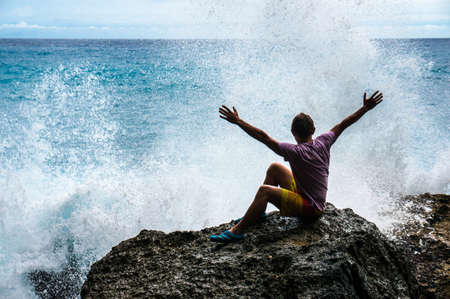 Young man with raised hands sitting on the rockの写真素材