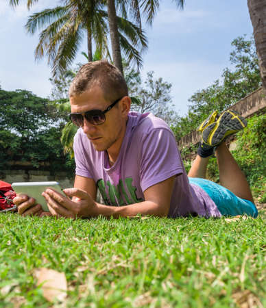 Man laying on the grass and using his tablet