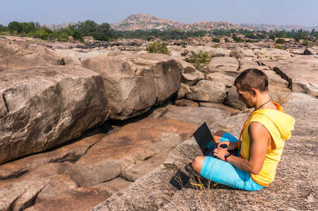 Young man sitting on the mountain with beautiful view and working on his laptopの写真素材
