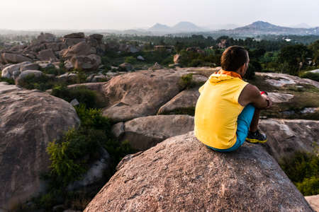Young man sitting alone on the edge of mountain and looking forwardの写真素材