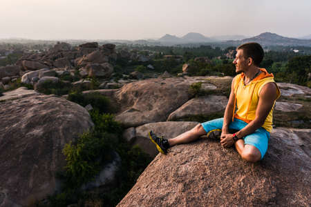 Young man is sitting on the mountain with beautiful view and looking aroundの写真素材