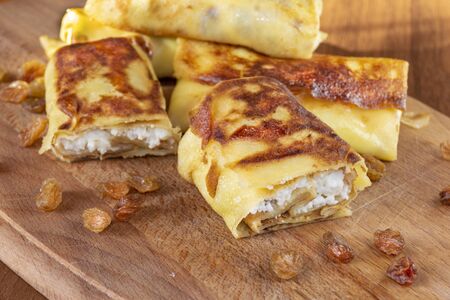 Pancakes with curd filling and raisins on a dish on an old wooden surfaceの写真素材