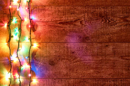 Christmas lights or Colorful garland on the left on a wooden background. Bright and colorful New Year festive decorations with glowing Christmas lights. Flat lay, top view, horizontal layoutの写真素材