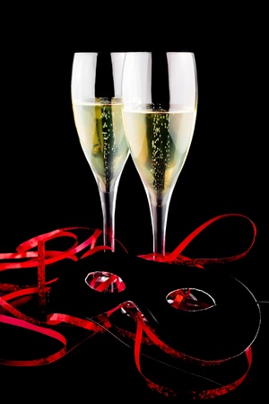 two flutes with champagne near a carnival mask on black backgroundの写真素材