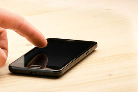 closeup of hand touching screen of black smartphone on wood desk