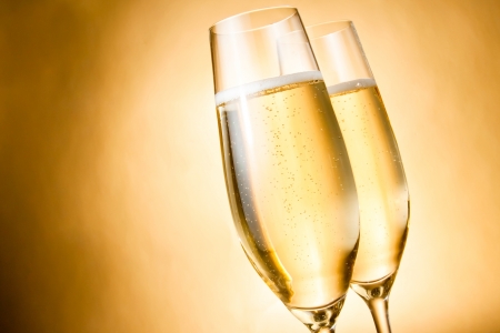 two glasses of champagne with golden bubbles against golden backgroundの写真素材