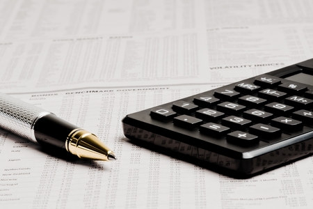 detail of a business pen near a calculator on financial newspaperの写真素材