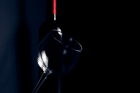 wine glass in front of bottle near its shadow on dark blue light with space for textの写真素材