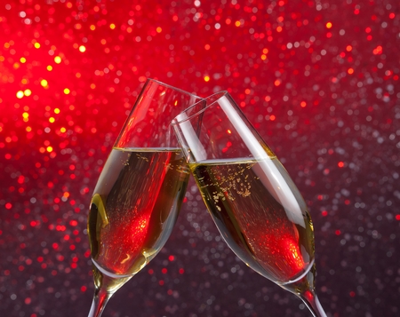 pair of a champagne flutes with gold bubbles make cheers on red and violet light bokeh backgroundの写真素材
