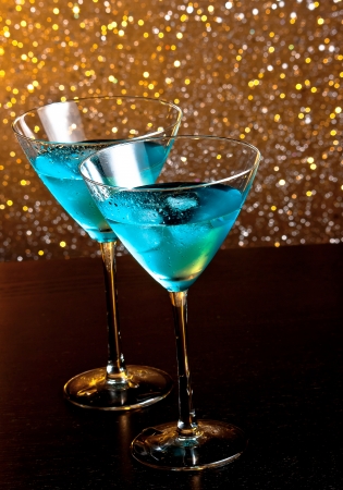 two glasses of fresh blue cocktail with ice on golden tint light bokeh background on wood tableの写真素材