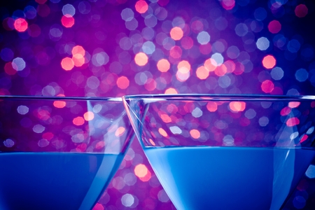 detail of a pair of glasses of blue cocktail on blue and violet tint light bokeh background with space for textの写真素材