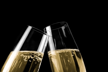a pair of champagne flutes with golden bubbles make cheers on black light background with space for textの写真素材