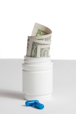 detail of blue pills in front of container with inside rolled up dollars on white background with space for textの写真素材