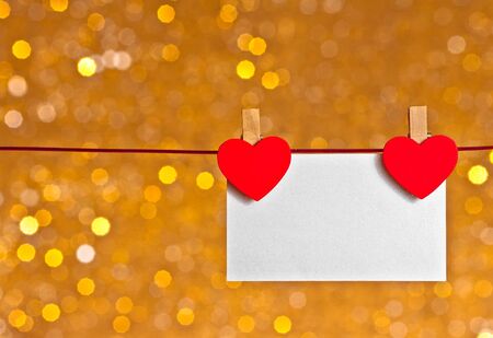 two decorative red hearts with greeting card hanging on golden light bokeh backgroundの写真素材