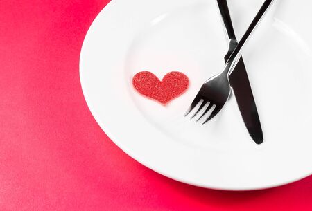 decorative red heart near a fork and knife on flat on red table with space for text, concept valentine day dinner の写真素材