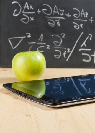 tablet pc and green apple in front of blackboard on wood table, concept of learn new technologyの写真素材