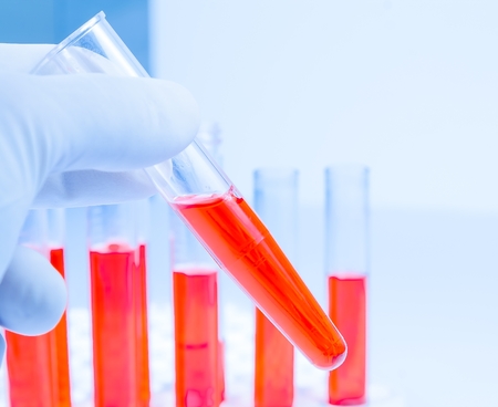 hand in glove is holding test tube with red liquid in laboratory isolated on white 