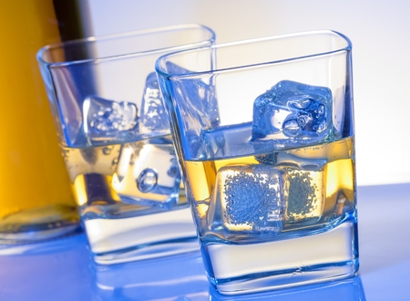 two glasses of whiskey with ice on blue light on white bar tableの写真素材
