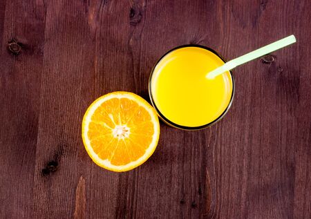 top of view of full glass of orange juice with straw and half orange on wood table with space for textの写真素材