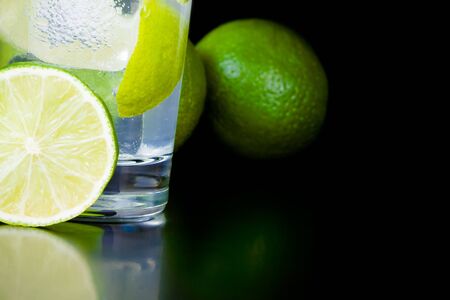 detail of lime slice near cocktail with ice on black background and space for text