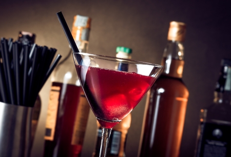 red cocktail into a glass with ice and  ice straw in front of bottlesの写真素材