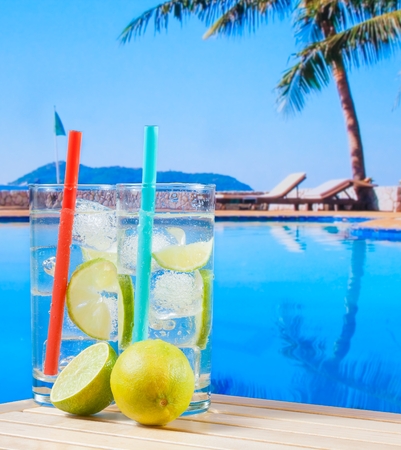 two glasses of cocktail with lime slice on blur swimming pool background on wood tableの写真素材