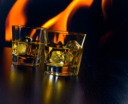 glasses of whiskey with ice cubes in front of the flame at nightの写真素材