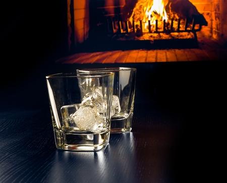 empty glasses of whiskey with ice cubes in front of the fireplace at nightの写真素材