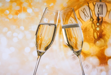 New Year or Christmas at midnight with champagne flutes make cheers, golden bokeh and clock on golden backgroundの写真素材