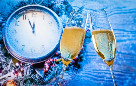 New Year or Christmas at midnight with champagne flutes with gold bubbles make cheers on blue light and clock backgroundの写真素材