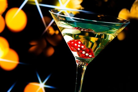 red dice in the cocktail glass on gold bokeh and stars backgroundの写真素材