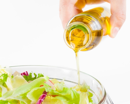 Extra virgin olive oil bottle pouring in the Italian fresh salad isolated on white background diet conceptの写真素材