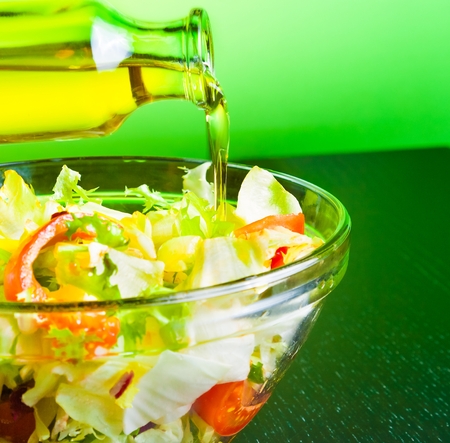 olive oil bottle pouring in the Italian fresh salad on green light tint background diet conceptの写真素材