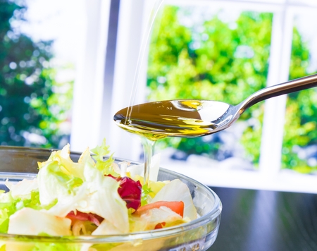 spoon with pouring olive oil on italian fresh salad on window background diet conceptの写真素材