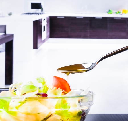 spoon with olive oil on italian fresh salad and tomato on kitchen background nutrition conceptの写真素材