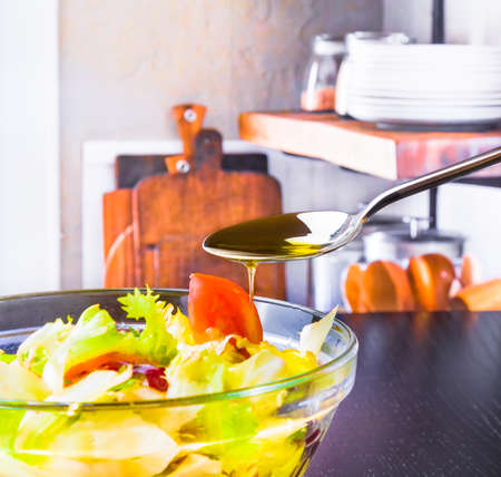 spoon with olive oil on italian fresh salad and tomato on kitchen background diet conceptの写真素材