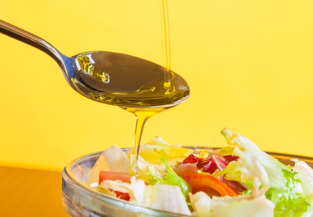spoon with olive oil on italian fresh salad on yellow light tint background diet conceptの写真素材