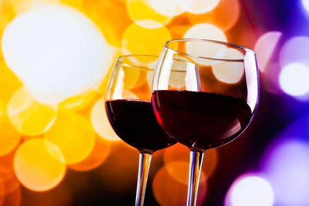 two red wine glasses against colorful bokeh lights background, festive and fun conceptの写真素材