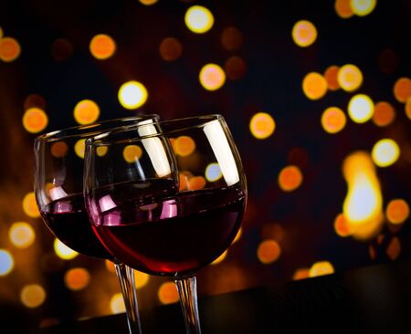 two red wine glasses on wood table against bokeh lights background, festive and fun conceptの写真素材