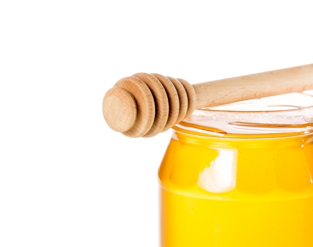 closeup of opened honey jar with wooden honey dipper on top isolated on white backgroundの写真素材