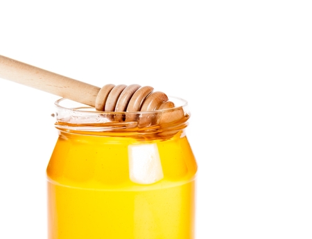 closeup of opened honey jar with wooden honey dipper inside, isolated on white backgroundの写真素材