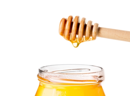 opened honey jar with wooden honey dipper on top with drop honey, isolated on white backgroundの写真素材