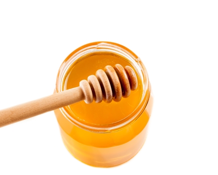 top of view of opened honey jar with wooden honey dipper on top, isolated on white backgroundの写真素材