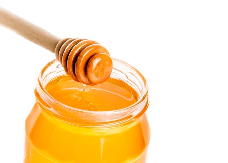 honey jar with wooden honey dipper on top, isolated on white backgroundの写真素材
